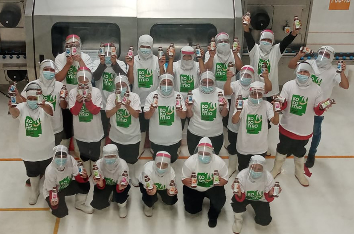20 happy factory workers holding up Kokomio bottles